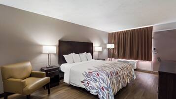 Ein Hotelzimmer mit Bett, Sessel, zwei Nachttischen mit Lampen, einem Fenster mit Vorhängen und einem Kleiderschrank.