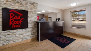 L'aire d'accueil d'un hôtel Red Roof Inn, avec un mur en pierre, un comptoir d'accueil et une vue sur la rue par une fenêtre.