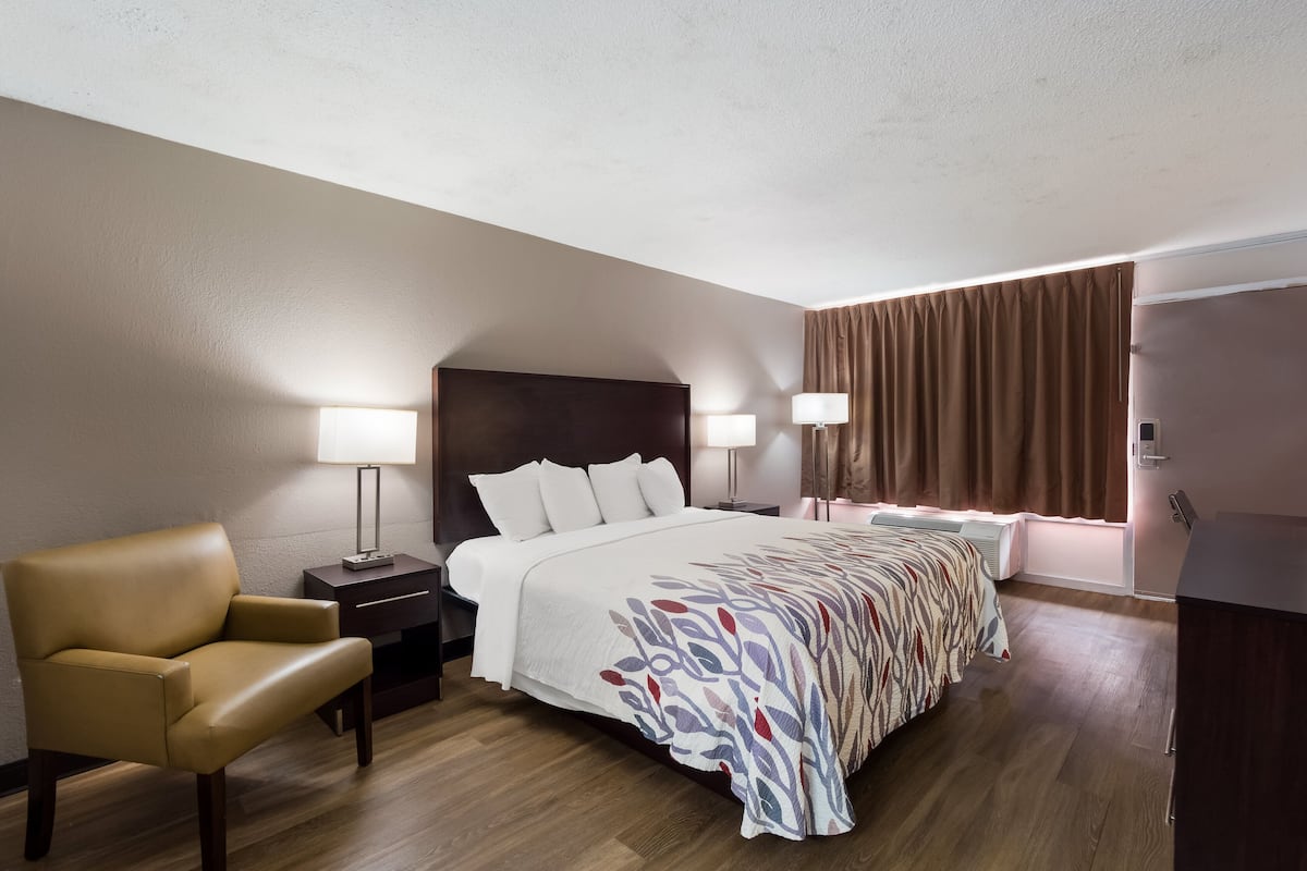 A hotel room with a large bed, a chair, two bedside tables, and a window with curtains.