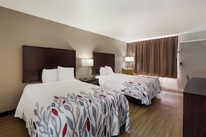 A hotel room with two beds, a nightstand, a lamp, a desk, and a door. - Red Roof Inn Columbia, SC Airport (West Columbia)