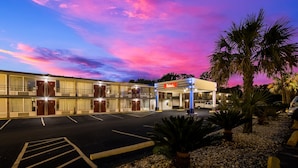 Un motel avec une station-service, un parking et des palmiers.