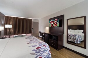 Habitación de hotel con una cama grande, un televisor de pantalla plana montado en la pared, un escritorio con una silla, un microondas y un refrigerador.