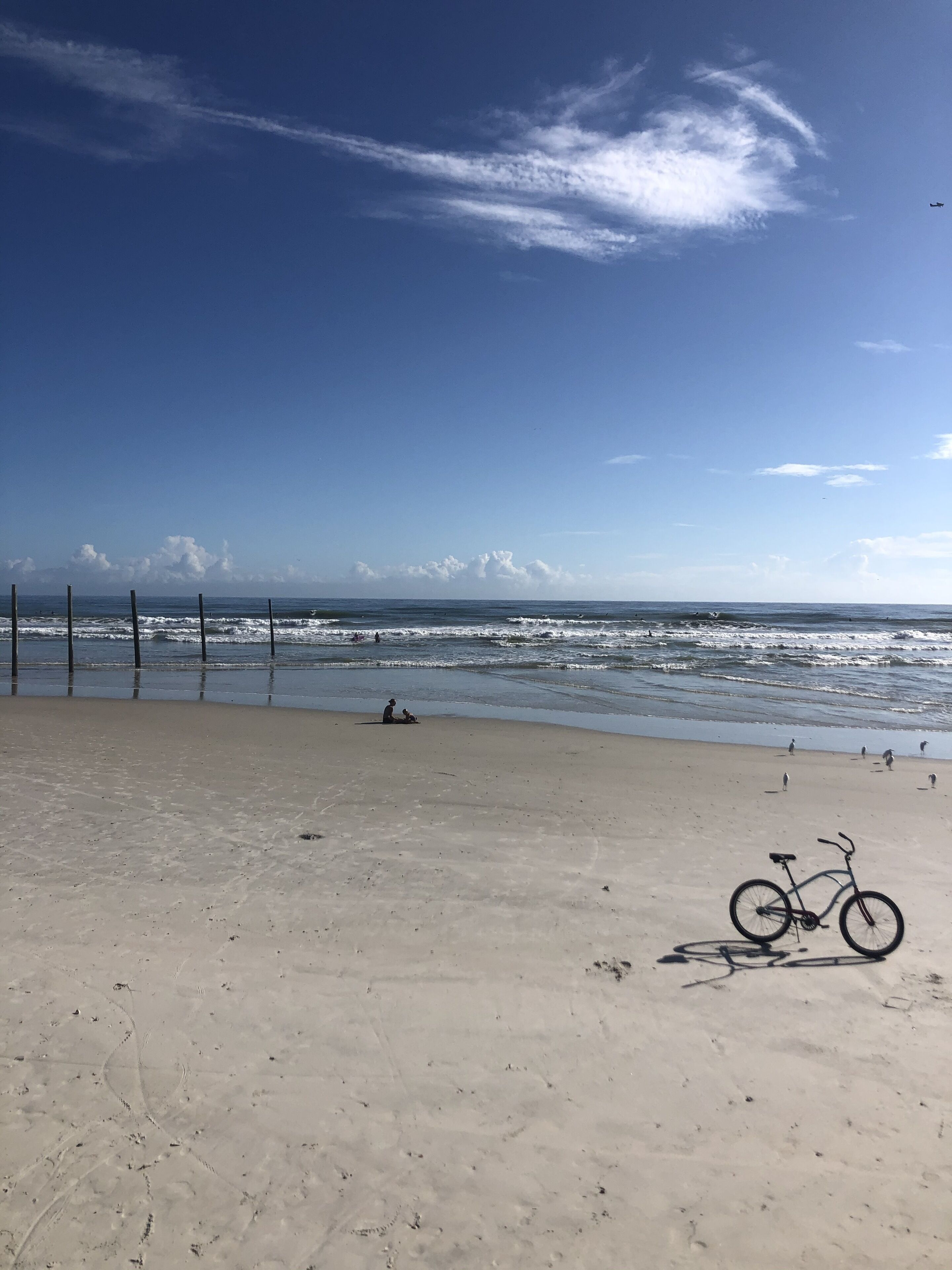 A sandy beach with a bicycle, a fence, and the ocean in the background.