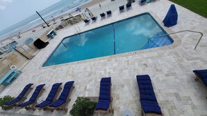 A swimming pool with lounge chairs and a view of the beach.
