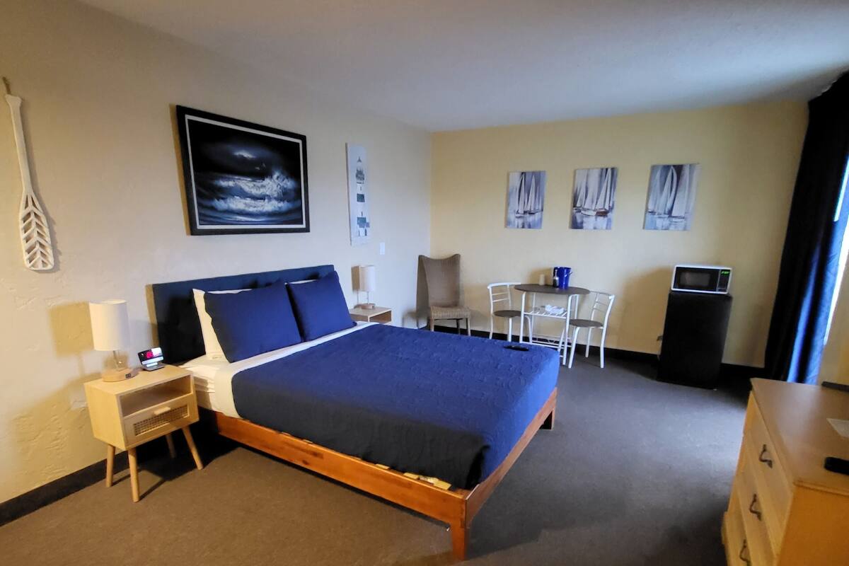 A hotel room with a bed, a desk, a chair, a dresser, and a microwave.