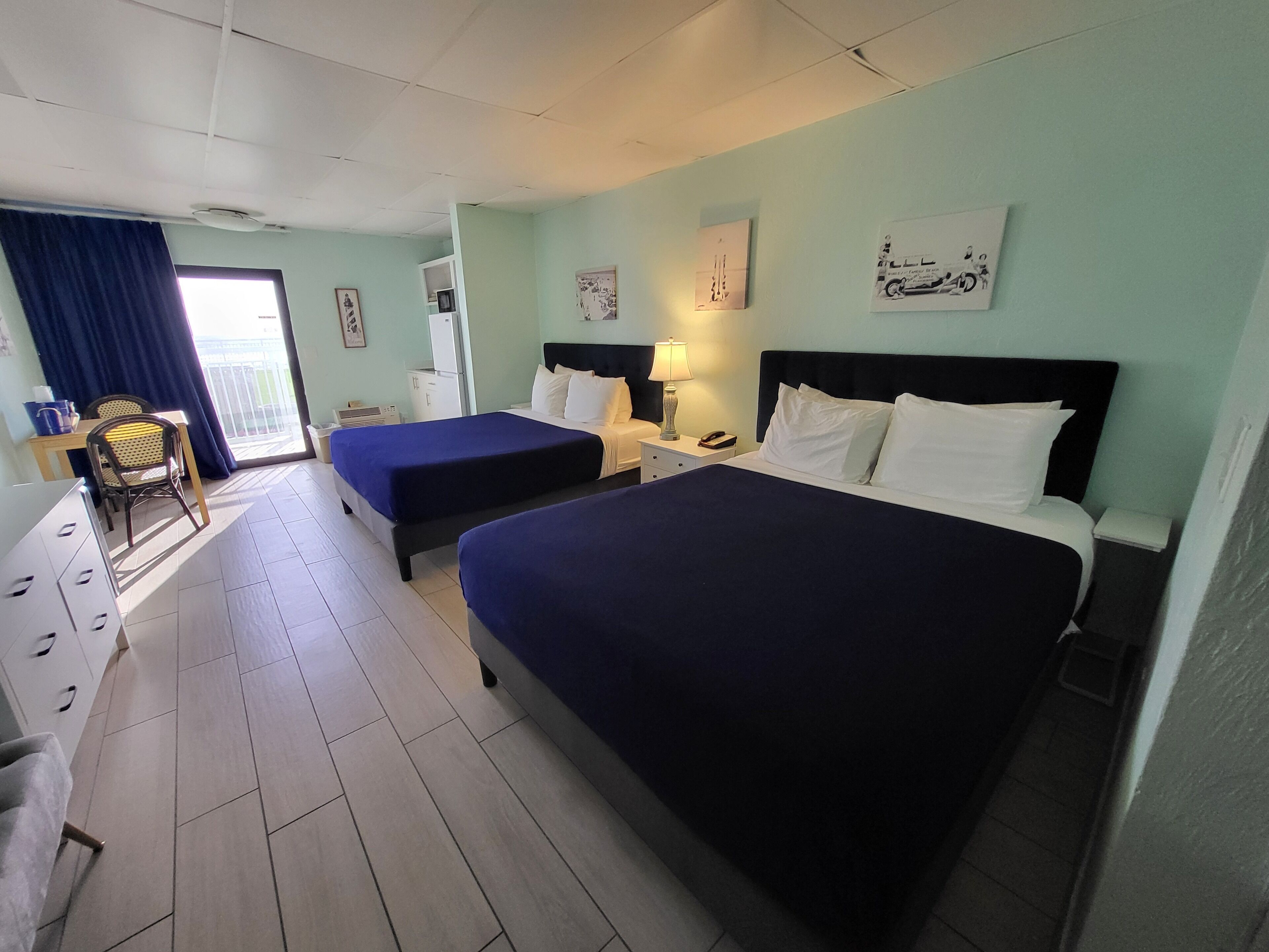 A hotel room with two beds, a desk, a chair, and a window with curtains.