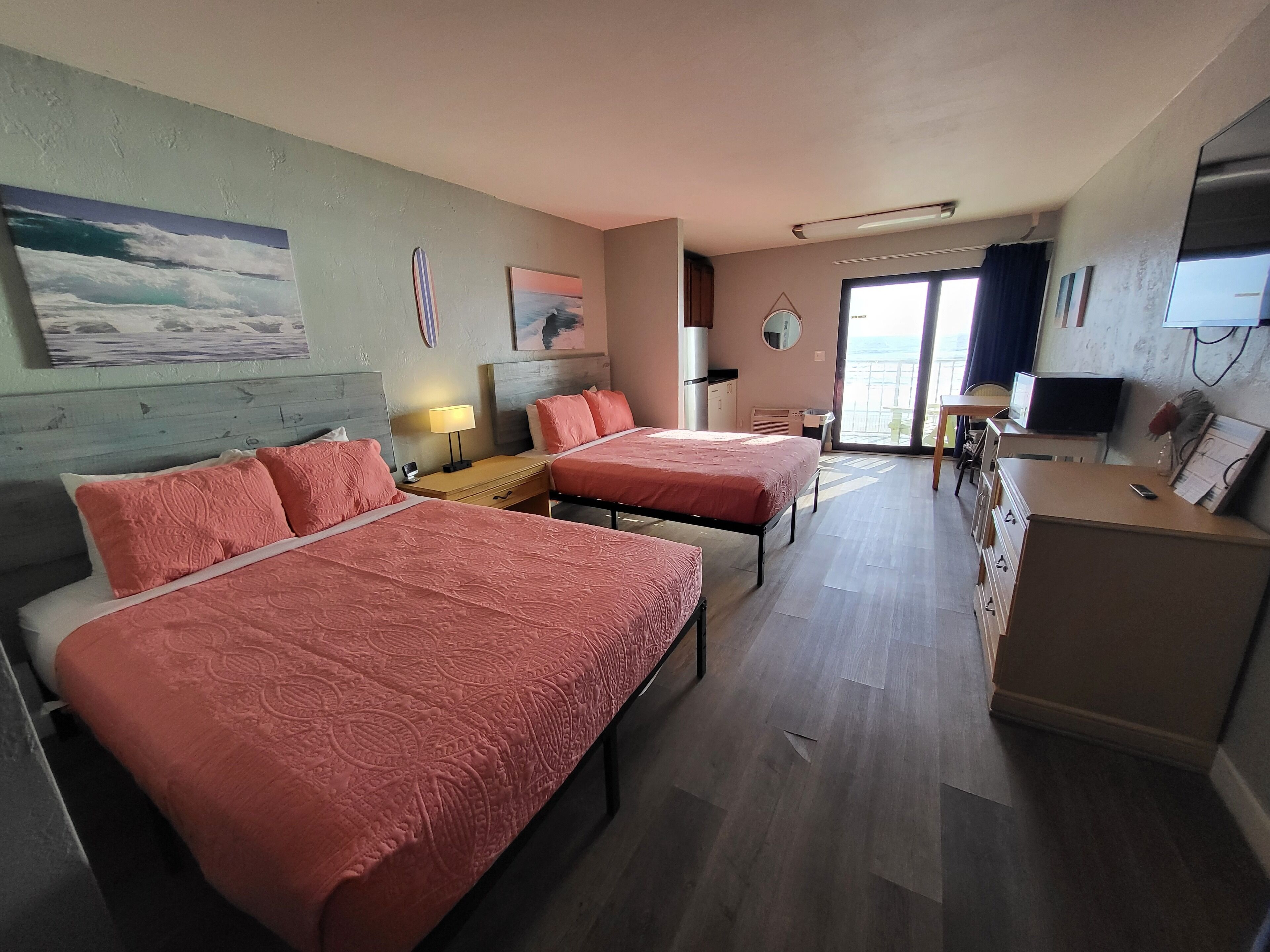 A hotel room with two beds, a desk, a chair, a TV, and a balcony with a view.