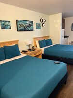 Una habitación de hotel con dos camas, una mesita de noche, una lámpara y cuadros en la pared.