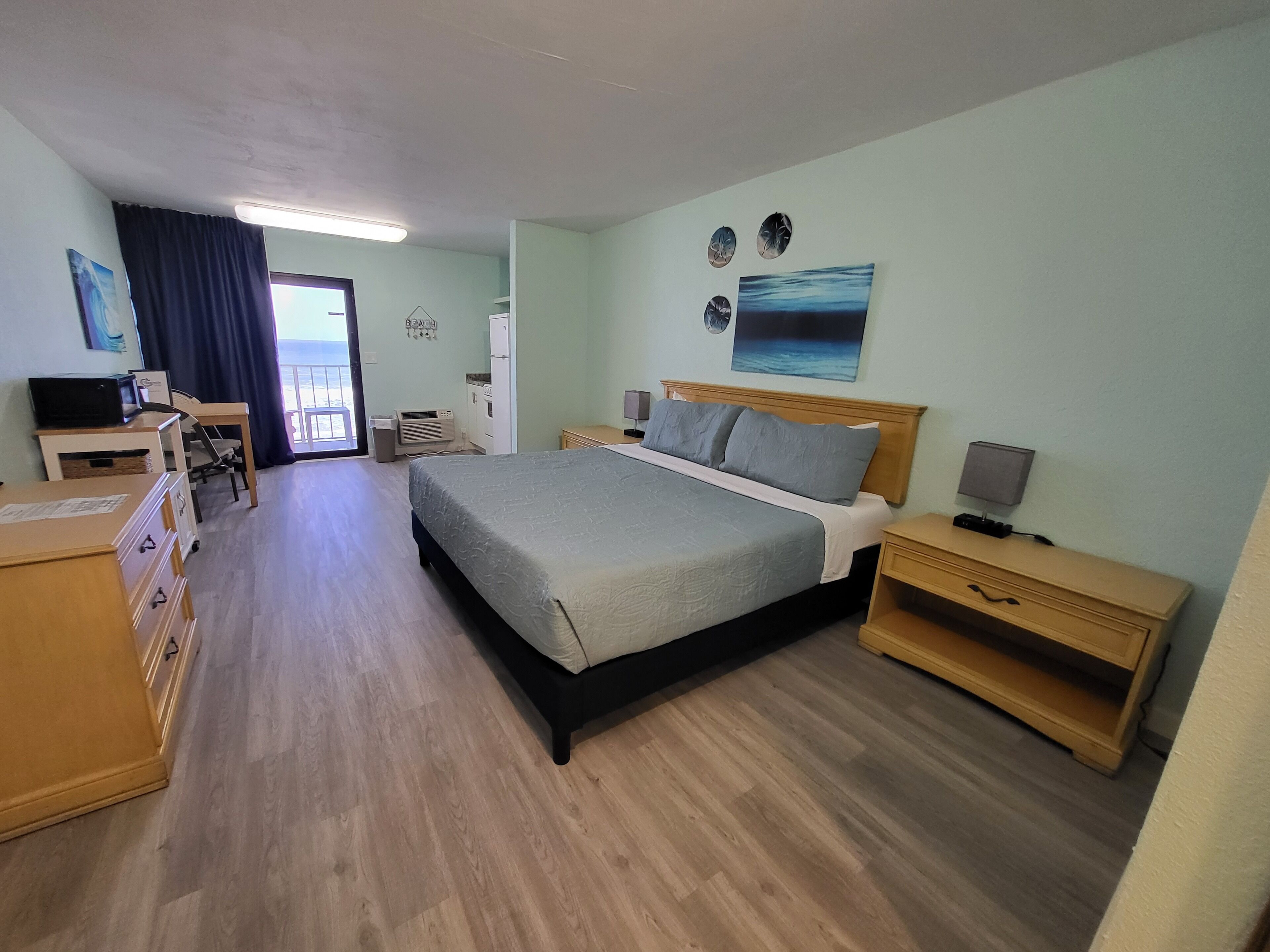 Una camera d'albergo con un letto, comodini, una scrivania con una sedia, una televisione e vista sull'oceano dalla finestra.