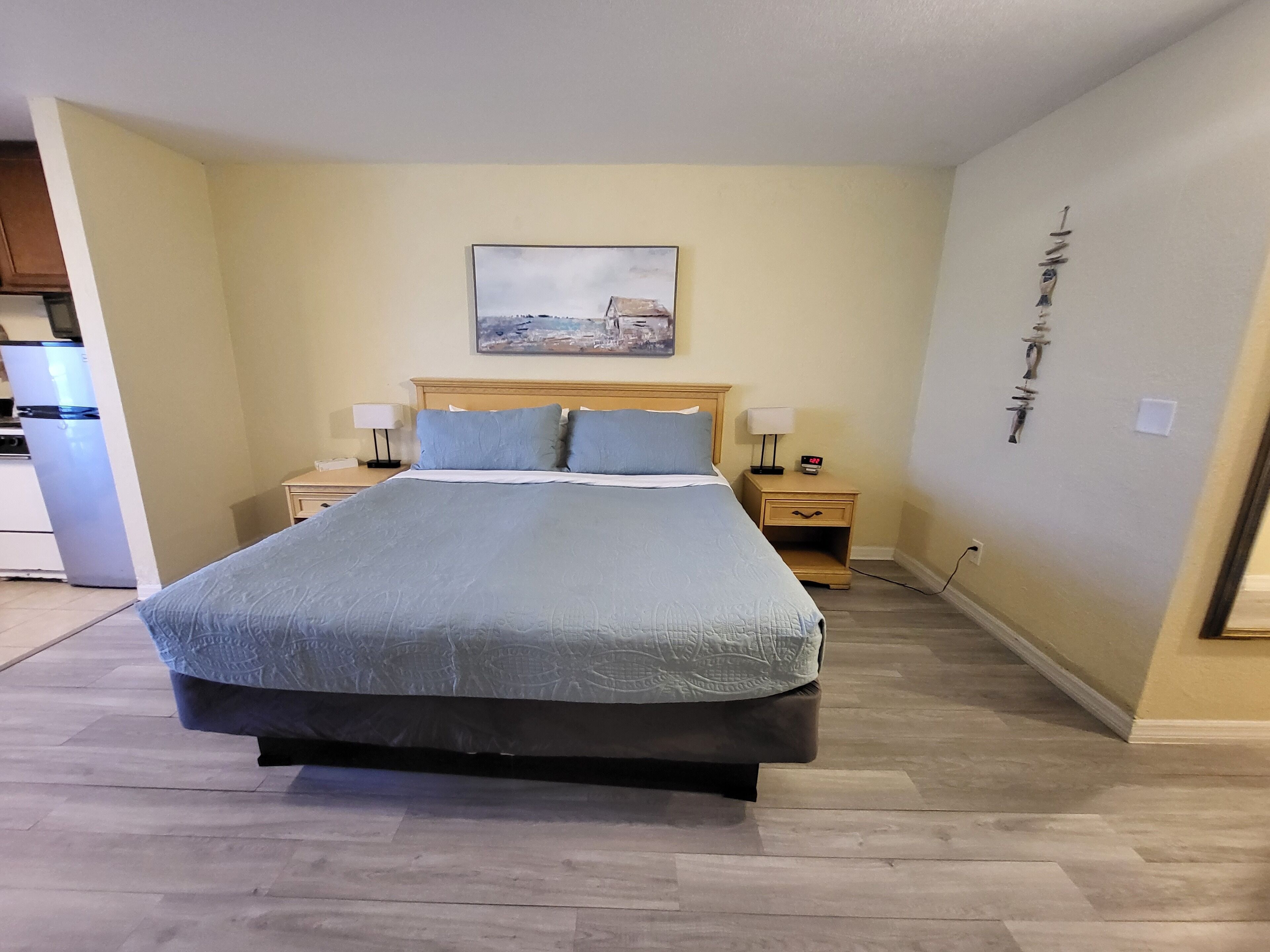 Une chambre à coucher bien aménagée, avec un grand lit, deux tables de chevet, une commode et une œuvre d’art accrochée au mur.