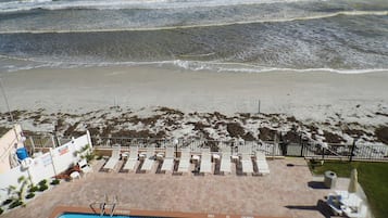A beach view with a pool area, sun loungers, and a fence.