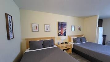 A hotel room with two single beds, a nightstand with a lamp, a poster on the wall, and a refrigerator.