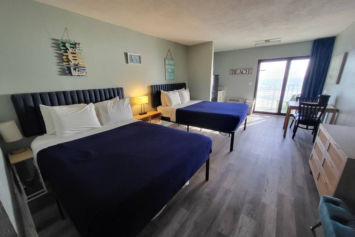 A hotel room with two beds, a desk, a chair, a window with a view, and a sign on the wall.