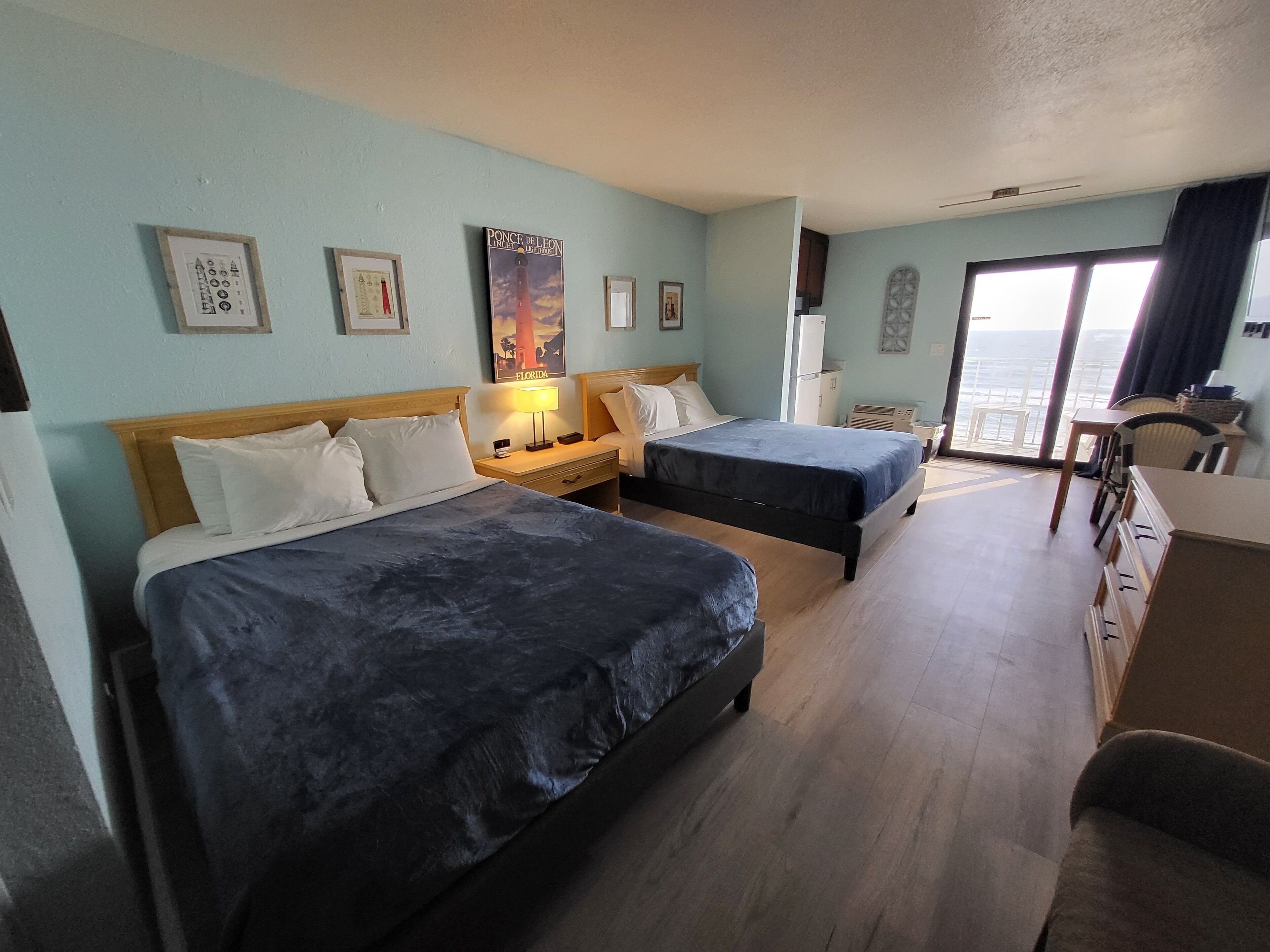 A hotel room with two beds, a desk, a chair, and a view of the ocean.
