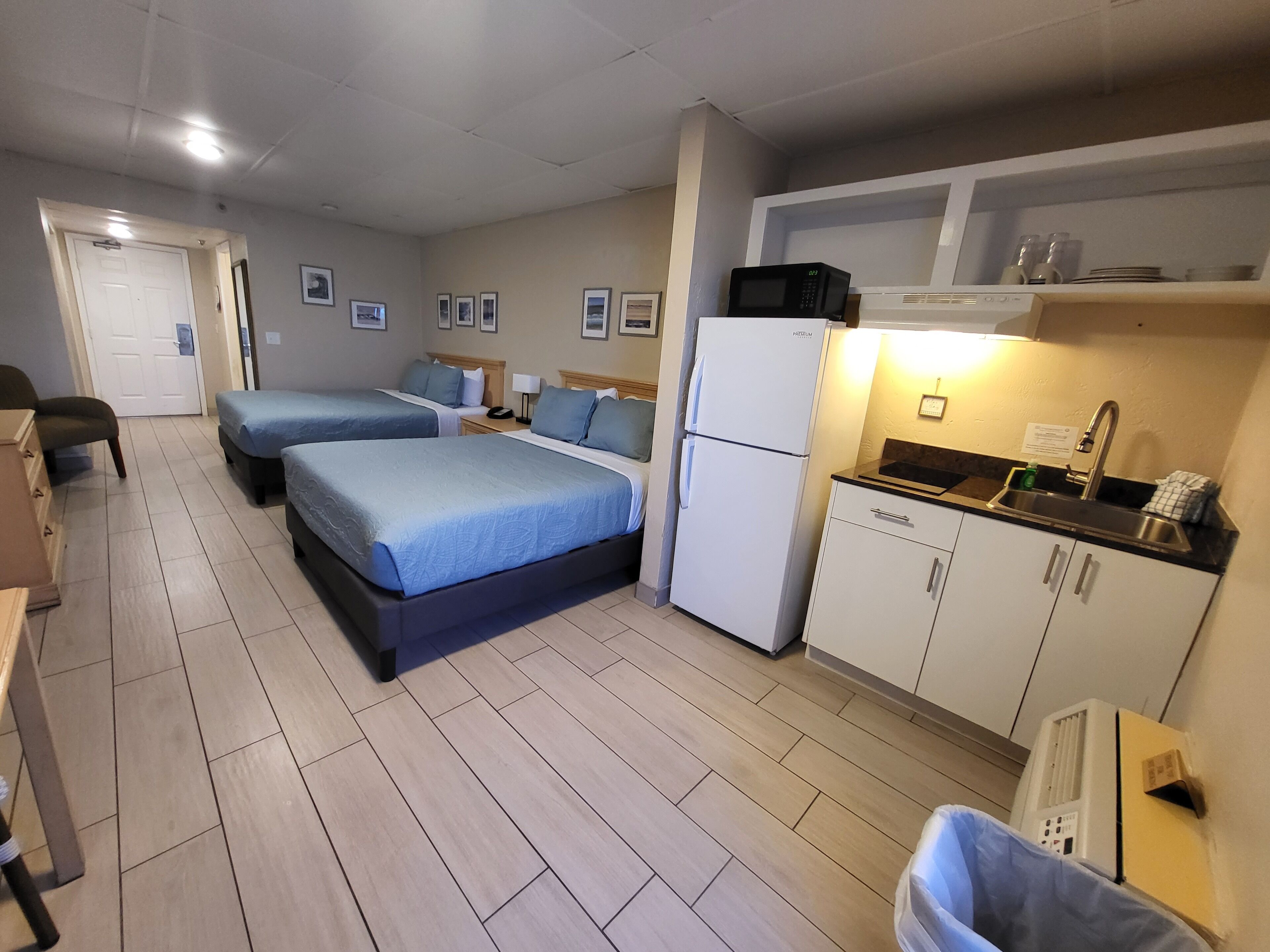 A hotel room with two beds, a kitchenette, a refrigerator, and a small bathroom.