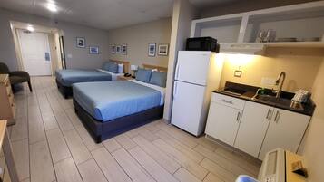 A hotel room with two beds, a kitchenette, a refrigerator, and a small bathroom.
