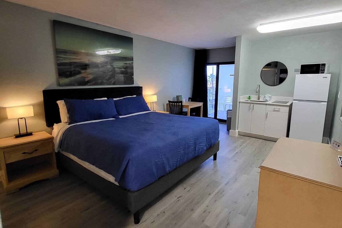 A hotel room with a bed, a desk, a refrigerator, and a window with a view.