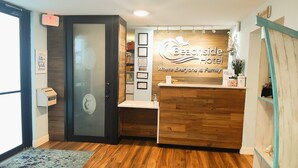 A reception area with a wooden reception desk, a glass door, and a sign that reads "Beachside Hotel Where Everyone Is Family."