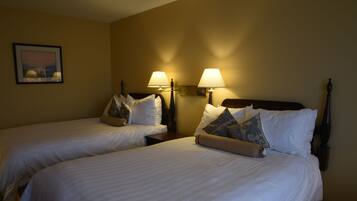 A hotel room with two beds, each with white linens and decorative pillows. There are wall-mounted lamps on either side of the beds.