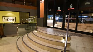 Un escalier incurvé et illuminé mène à un espace d’accueil doté d’une rambarde en verre.
