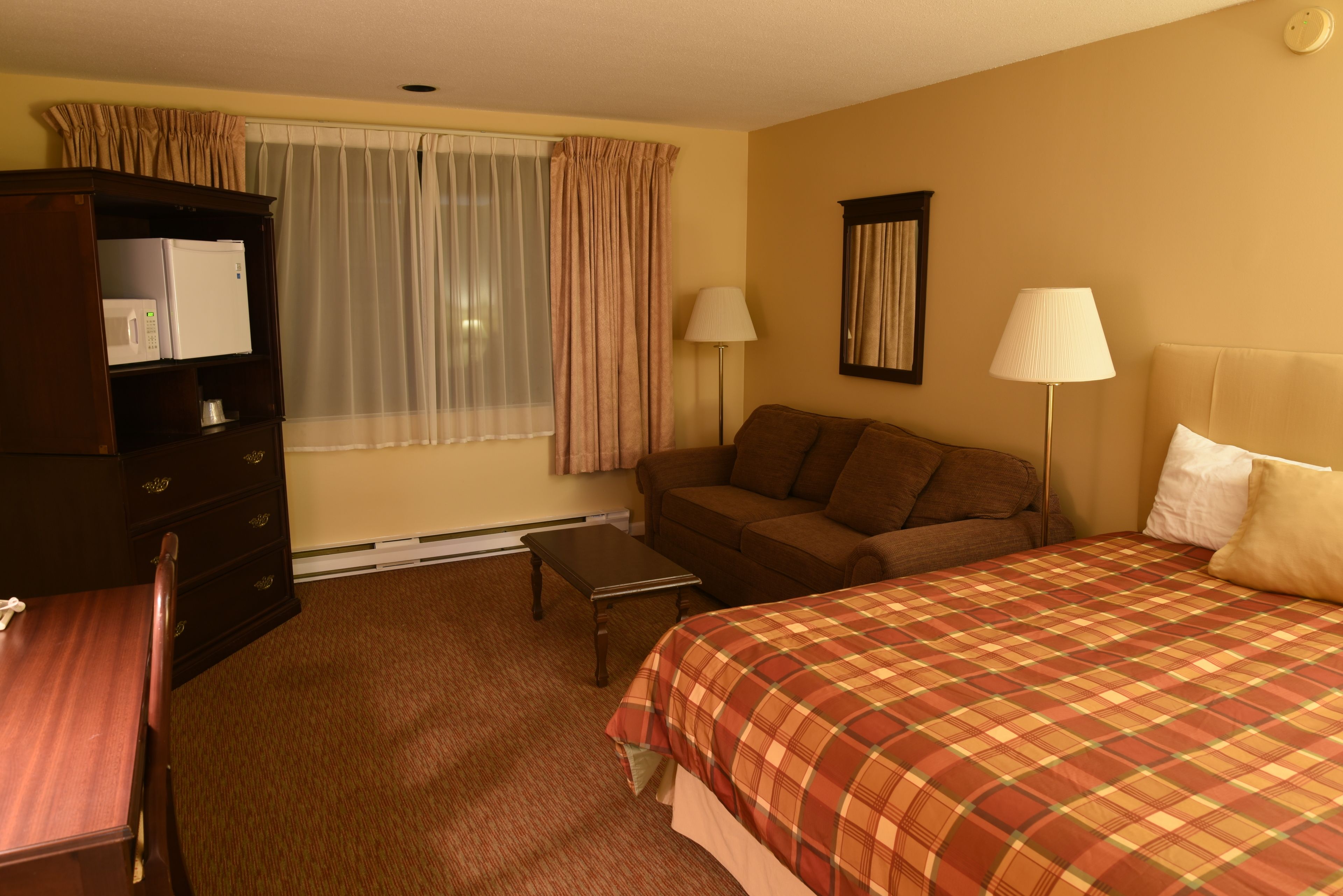 Una habitación de hotel con cama, sofá, escritorio, cómoda y ventana con cortinas.