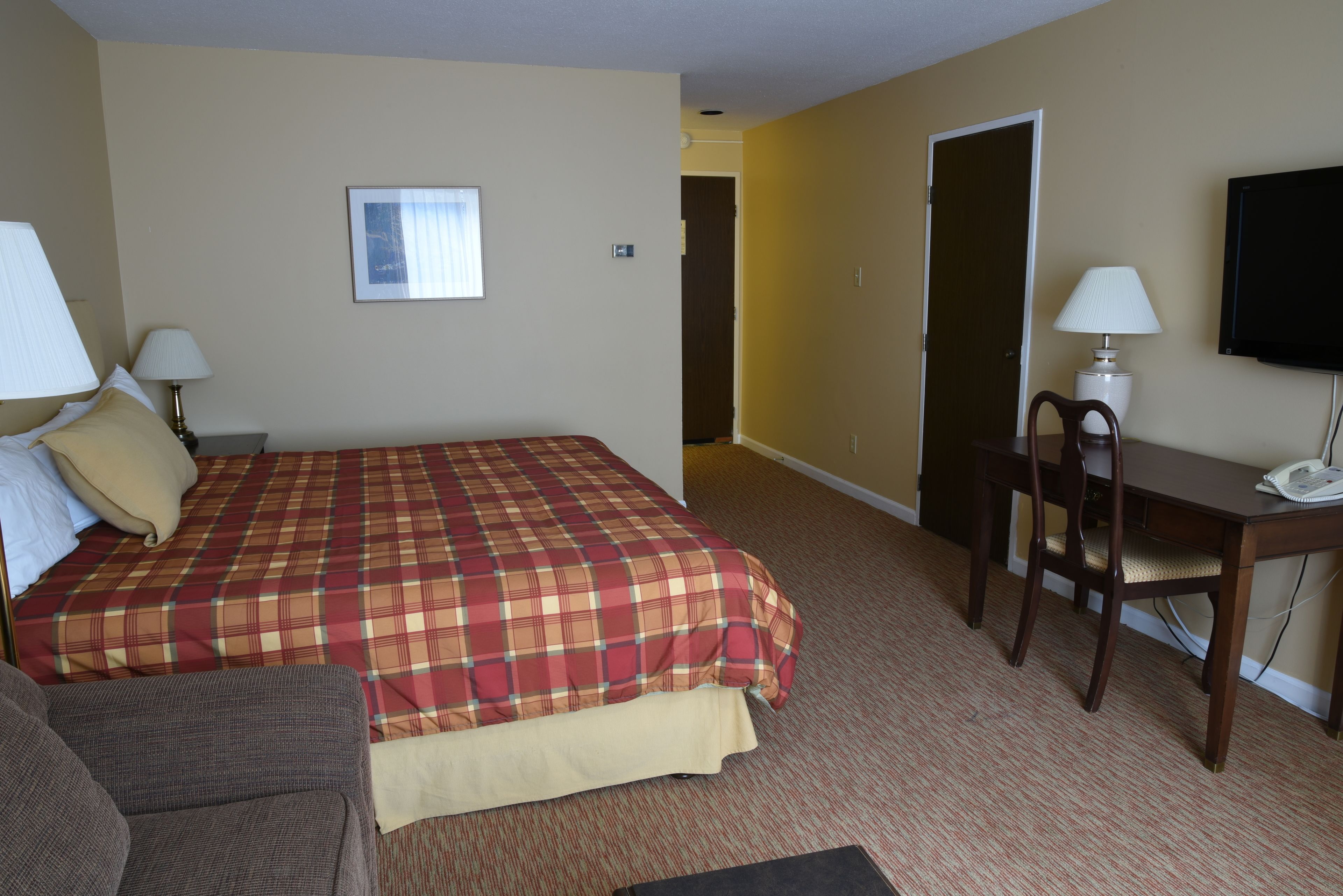 A hotel room with a large bed, a desk, a chair, and a television.