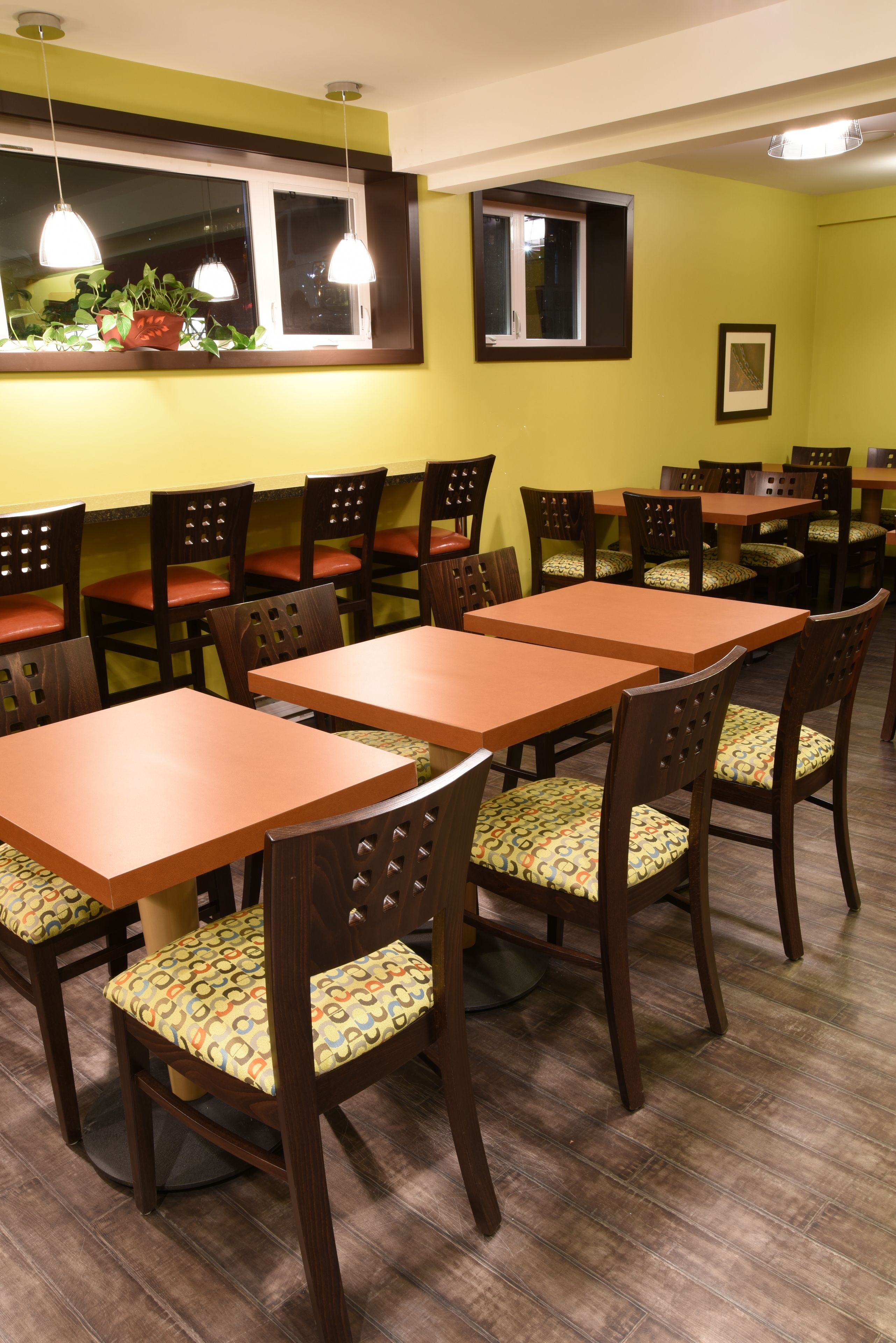 Interior de restaurante con varias mesas y sillas de madera, una ventana con vistas y lámparas colgantes.