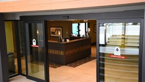 Un hall d'accueil d'hôtel doté de portes coulissantes automatiques, d'un comptoir de réception et dont l'intérieur est visible à travers les portes en verre.