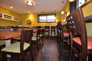 A dining area with wooden chairs and a table, yellow walls, and a window with natural light.