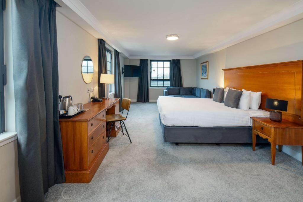 A hotel room with a large bed, a desk with a chair, a dresser, and a TV.