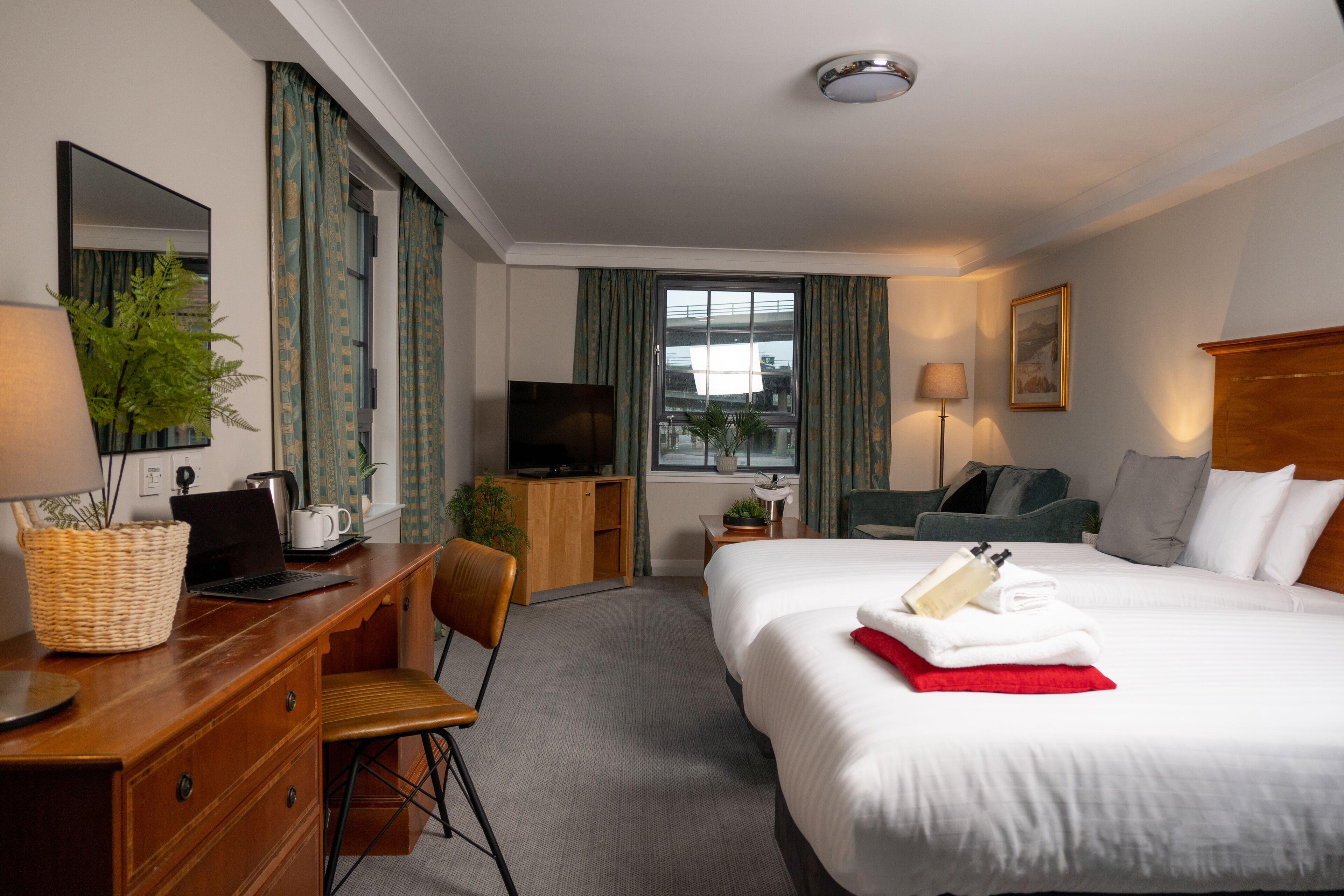 Une chambre d’hôtel avec un lit, un bureau, une chaise, une télévision et une fenêtre avec des rideaux.