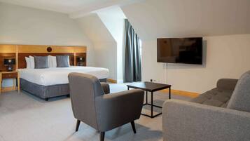Une chambre d’hôtel moderne équipée d’un lit, d’un bureau, d’une télévision et de deux fauteuils.