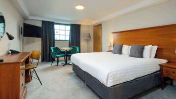 A hotel room with a large bed, a desk, a chair, a TV, and a window with curtains.