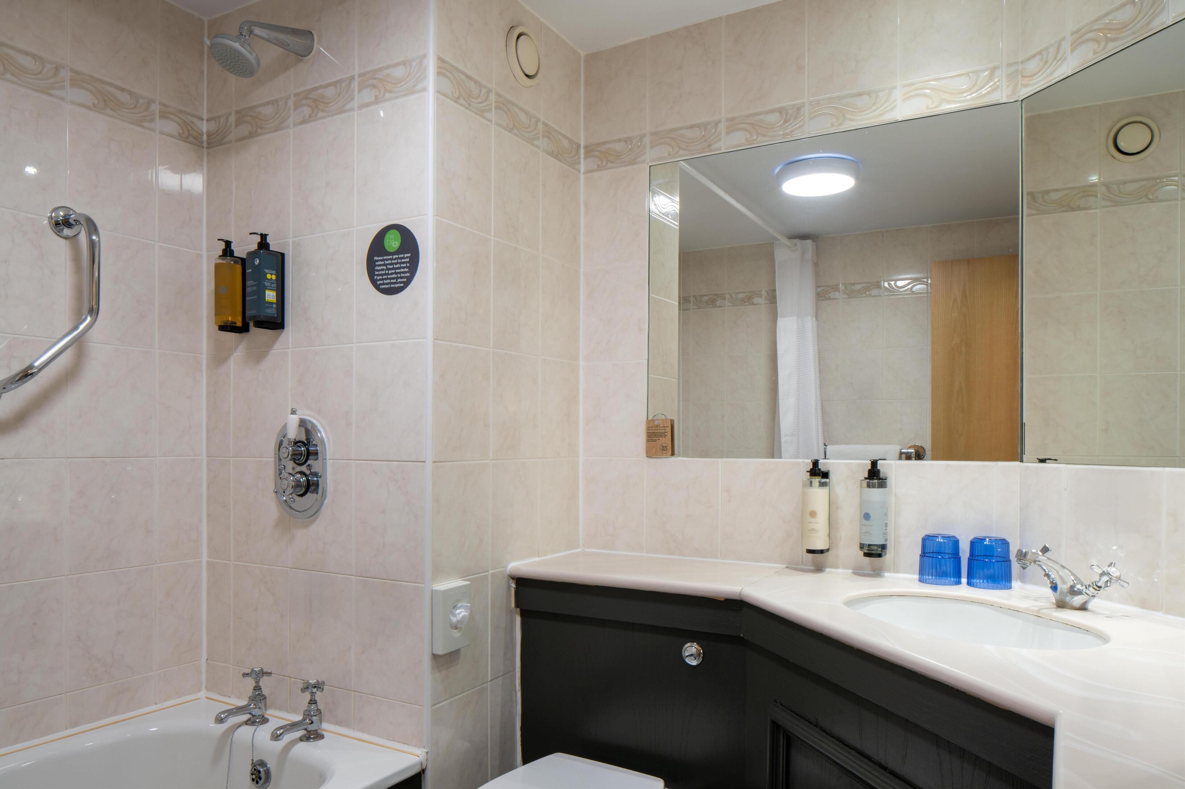 A bathroom with a bathtub, a shower, a sink with toiletries, and a mirror.