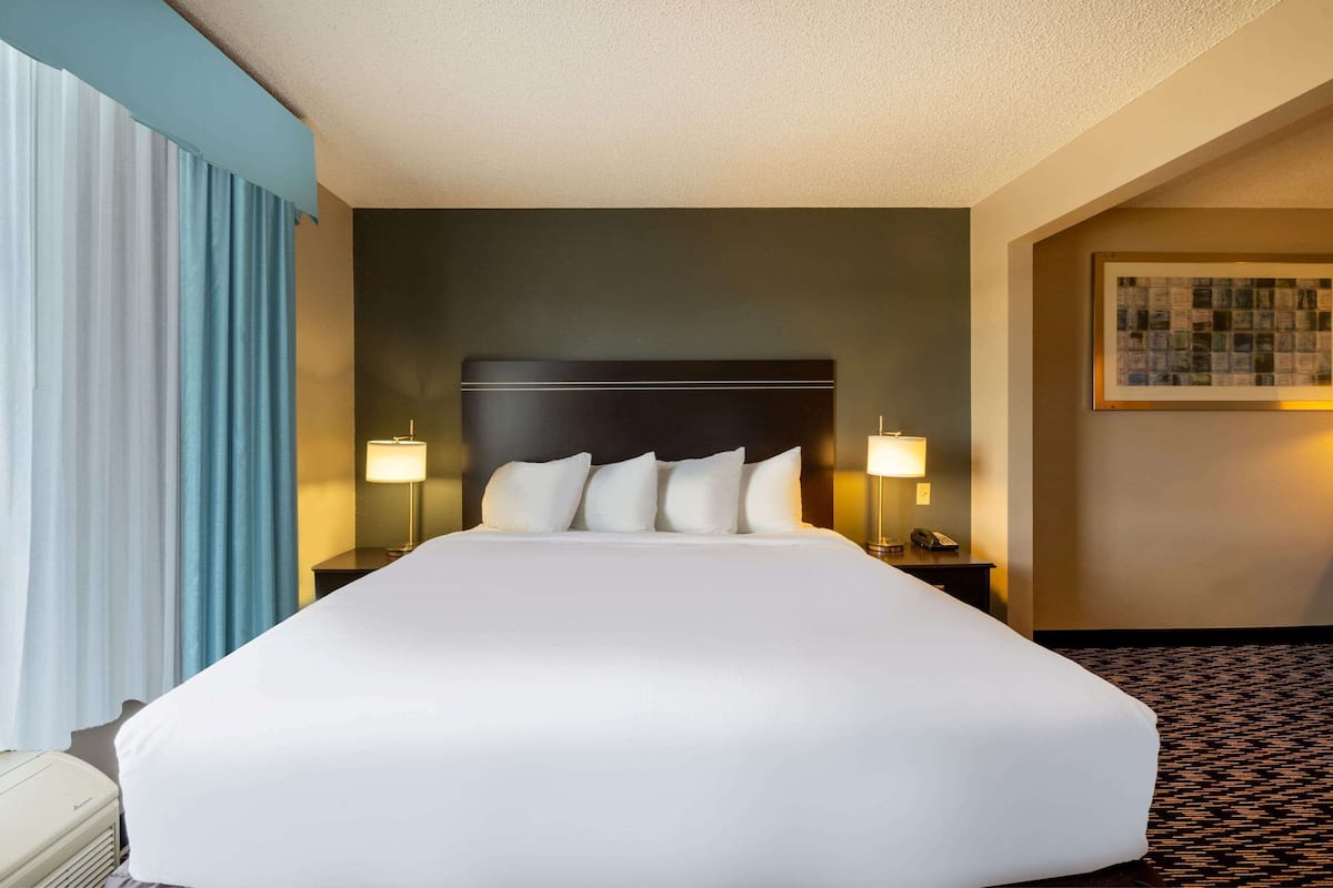 A hotel room with a large bed, two bedside tables with lamps, a headboard, and a framed picture on the wall.