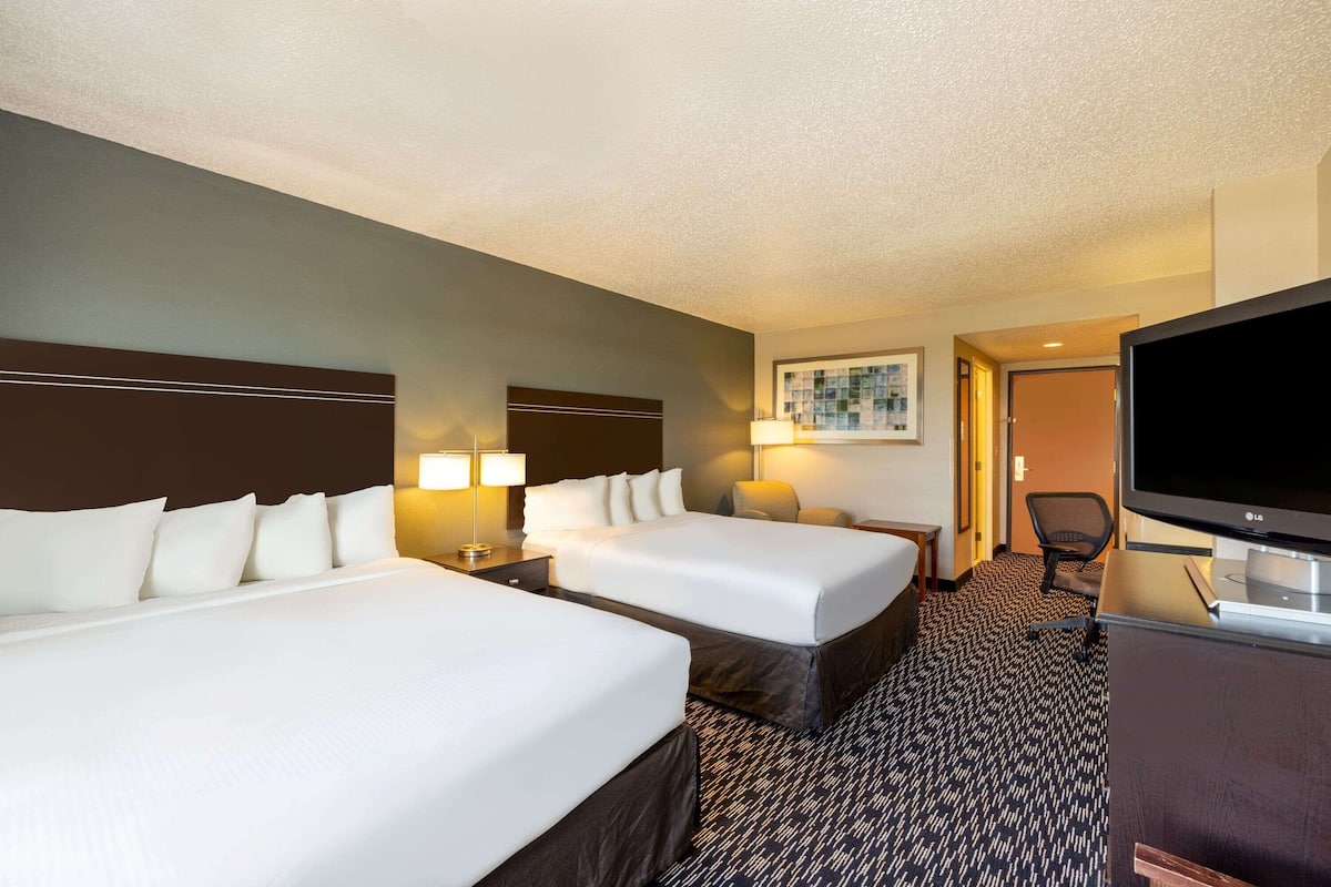 A hotel room with two beds, a TV, a desk, and a chair.