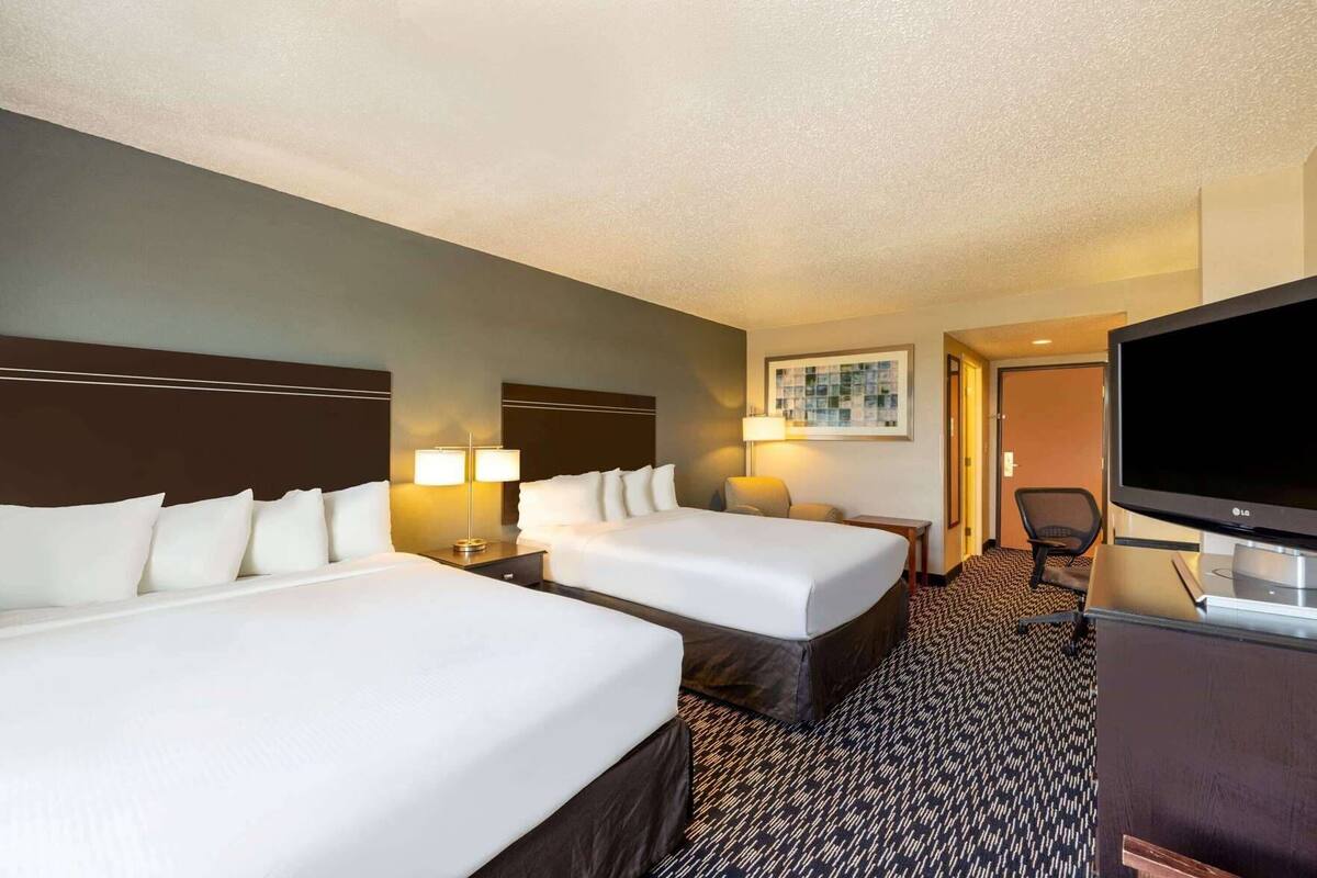 A hotel room with two beds, a television, a desk, and a chair.