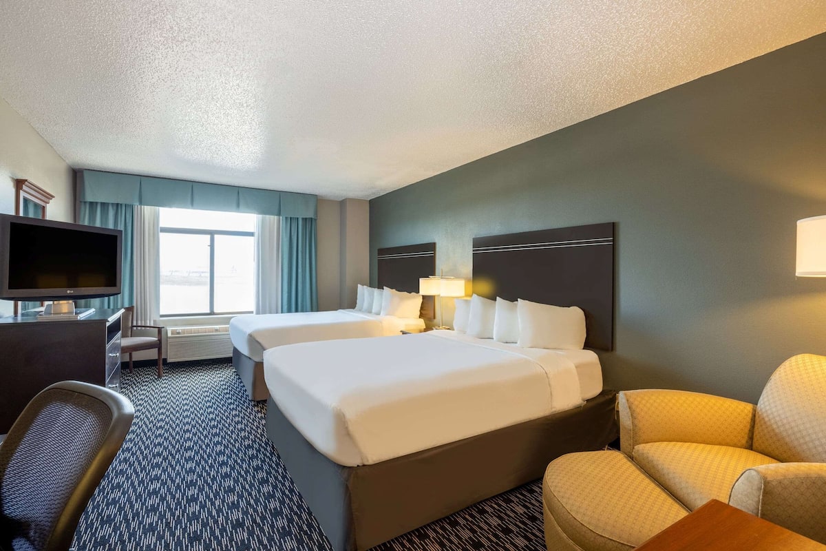 A hotel room with two beds, a desk, a TV, and a seating area.