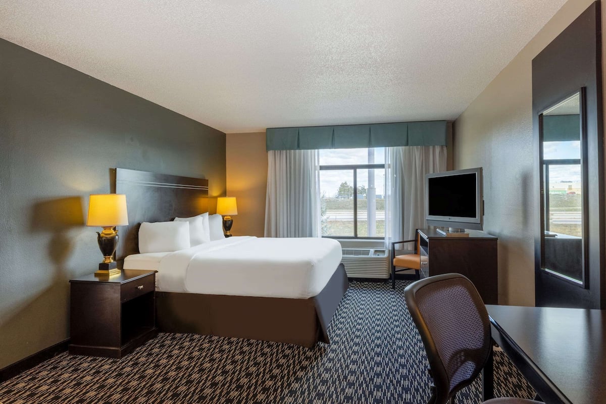 A hotel room with a bed, a desk, a chair, a TV, and a window with curtains.