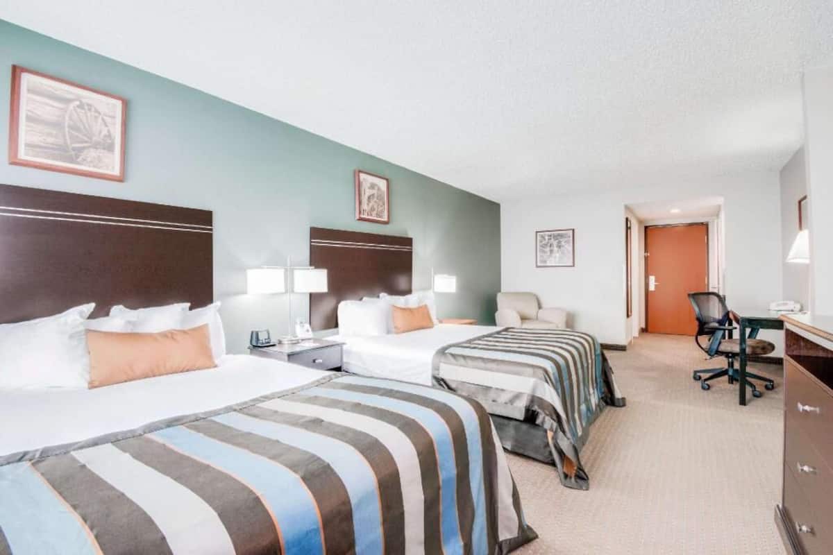 A hotel room with two beds, a desk, a chair, and a door.