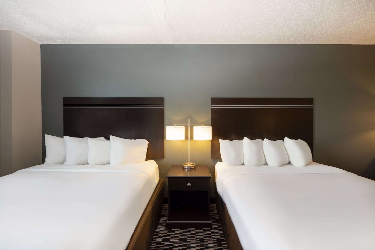 A hotel room with two beds, a nightstand with lamps, and a patterned rug.
