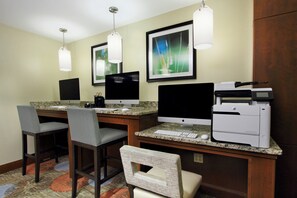A hotel room with two desks, each with a desktop computer, a printer, and a keyboard. There are two chairs, one grey and one white, and a carpeted floor. - Staybridge Suites Tysons - McLean by IHG (McLean)