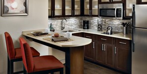 A modern kitchen with dark wooden cabinets, a stainless steel refrigerator, a microwave, and a coffee maker. - Staybridge Suites Tysons - McLean by IHG (McLean)