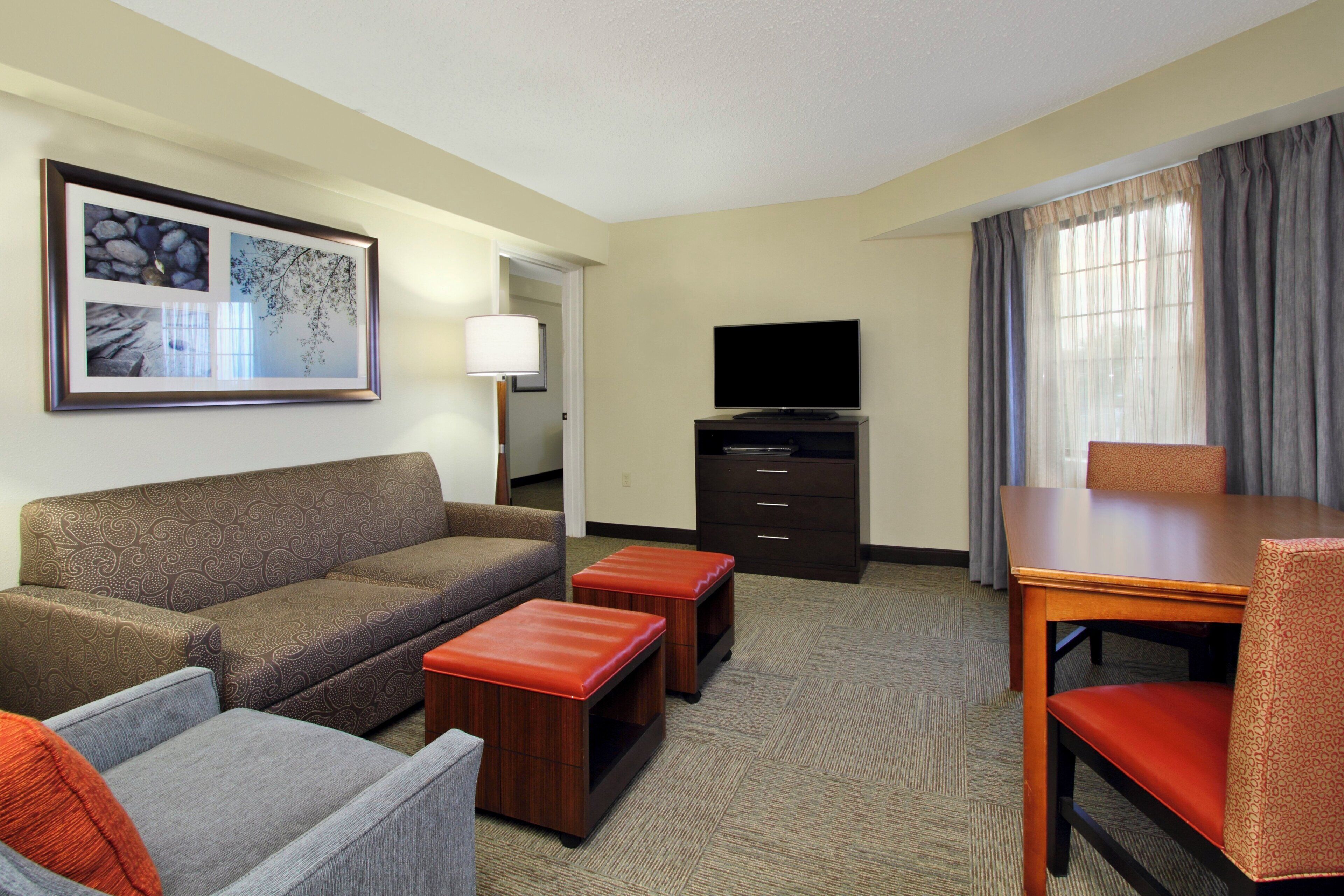 Habitación de hotel con sofá, dos otomanas, televisor, mesa y una silla.
