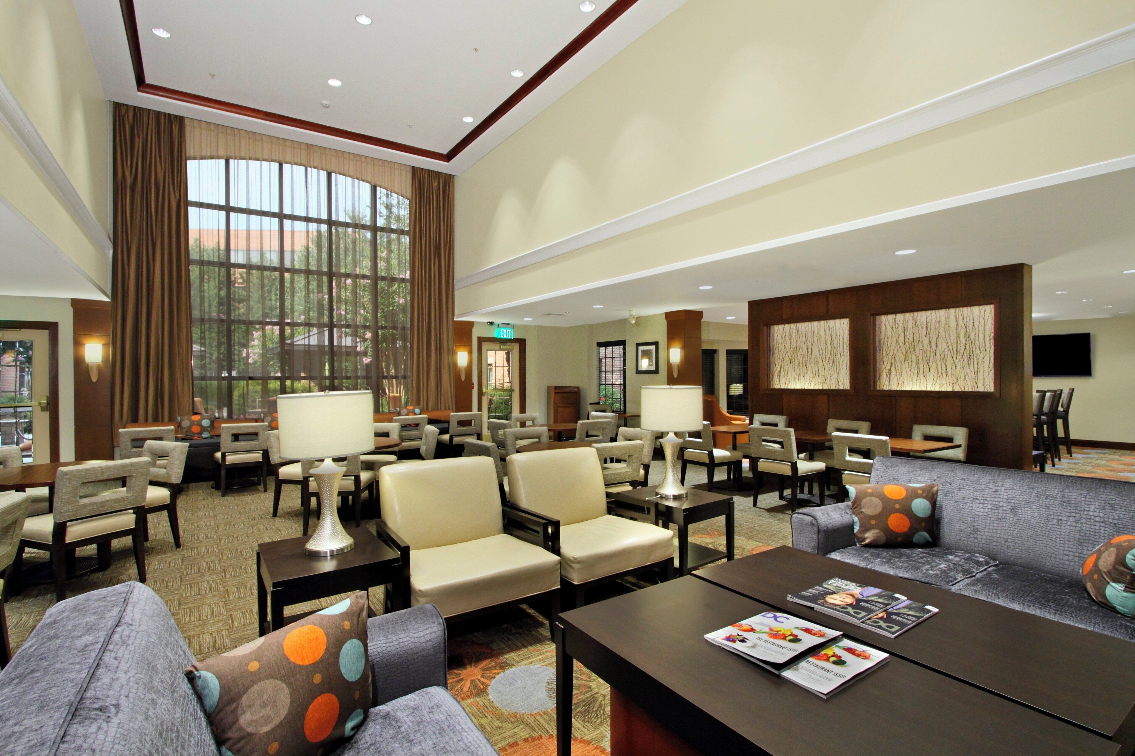 A spacious lobby with multiple seating areas, including sofas and chairs, a reception desk, and a large window providing a view of the outdoors.