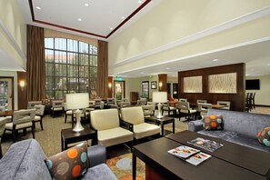 A spacious lobby with multiple seating areas, including sofas and chairs, a reception desk, and a large window providing a view of the outdoors. - Staybridge Suites Tysons - McLean by IHG (McLean)