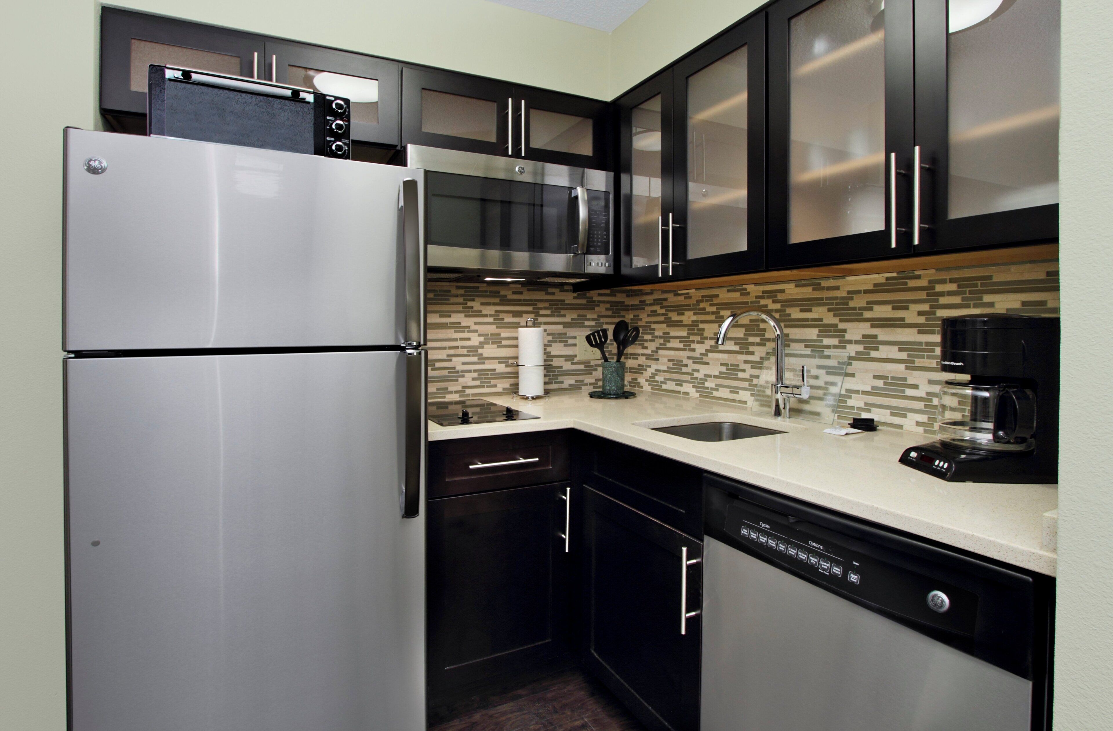 A modern kitchen with stainless steel appliances, black cabinets, a tiled backsplash, and a dishwasher.