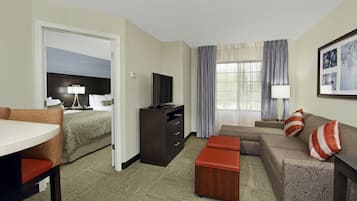 A hotel room with a bed, a TV, a desk, a sofa, and a window with curtains.