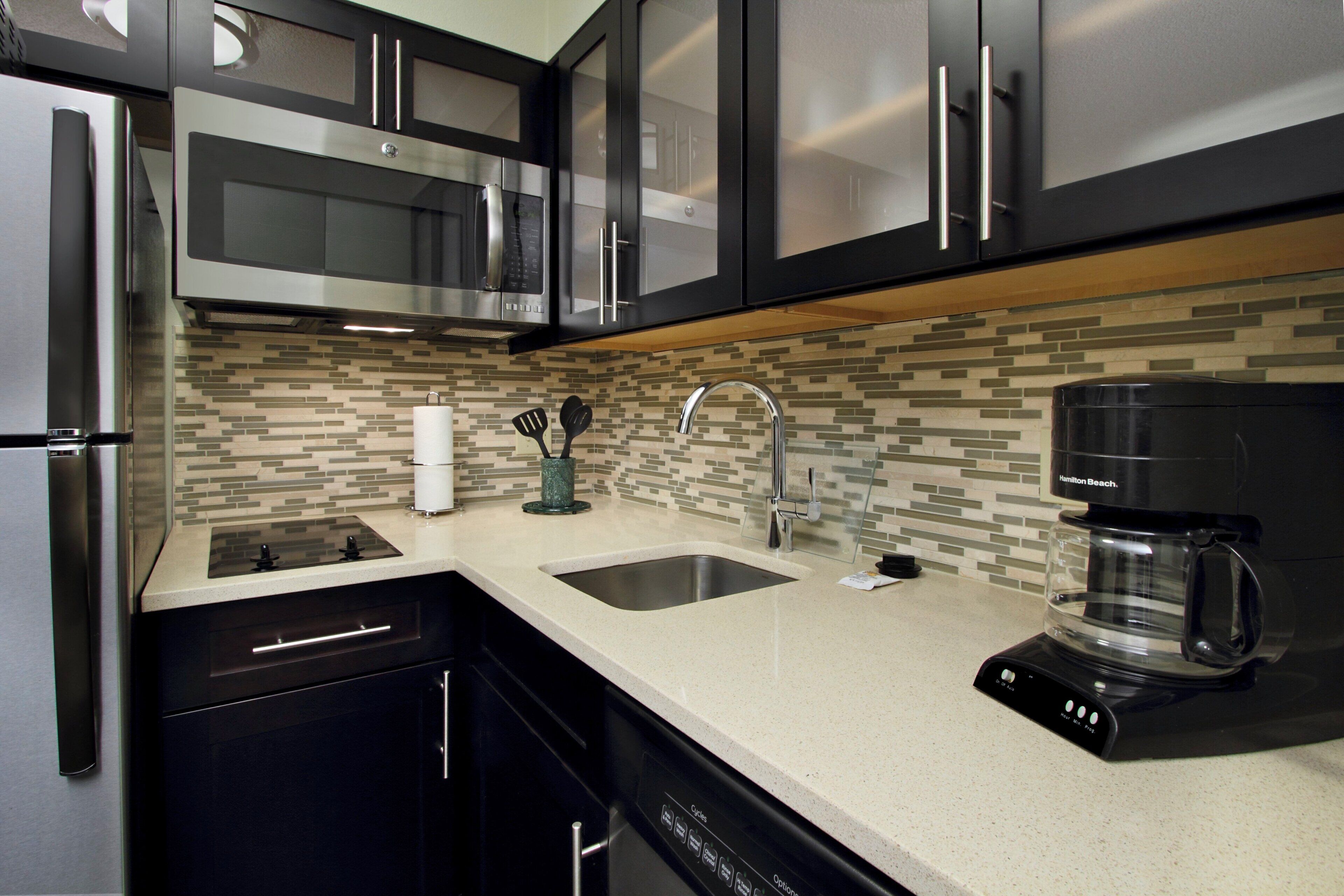 A modern kitchen with stainless steel appliances, a coffee maker, and a tiled backsplash.