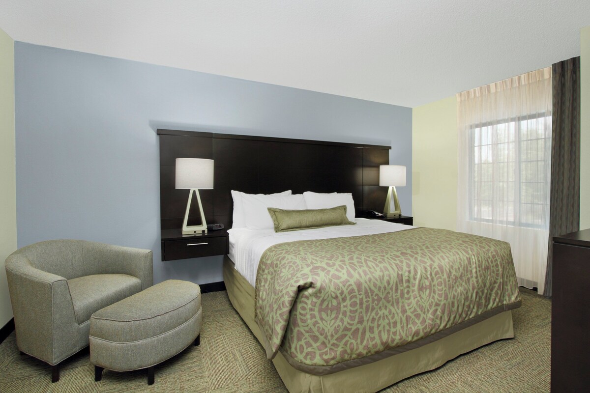 A hotel room with a bed, two bedside tables, a chair, and a window.